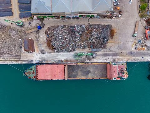 Cargo ship loading at a dock near a scrapyard in a busy industrial area dur.. Stock Photos