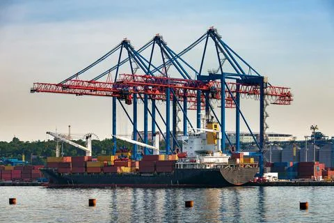 A cargo ship moored for loading at container yard with large cranes. Stock Photos