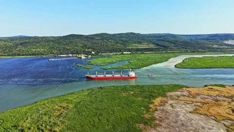 Cargo ship navigates river waterway with green banks and hills in background Stock Footage 341032352