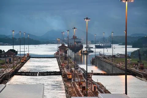 Cargo Ship Navigating Panama Canal Locks at Dusk with Illuminated Poles Stock Photos