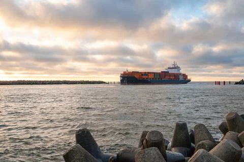 Cargo ship navigating through a rocky harbor entrance under a cloudy sky, s.. Stock Photos