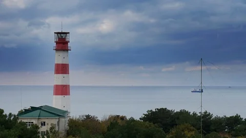 Cargo ship passes by a beautiful majestic lighthouse under dramatic stormy Stock-Footage 69791663