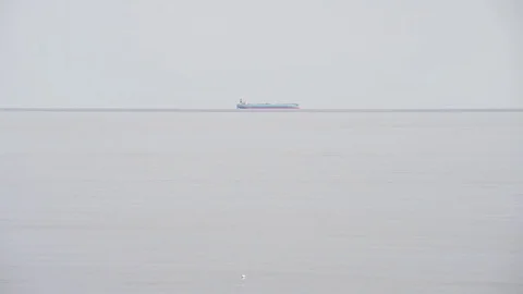 Cargo ship passes on the horizon while a drone flies over the beach on misty day Stock Footage 82963061