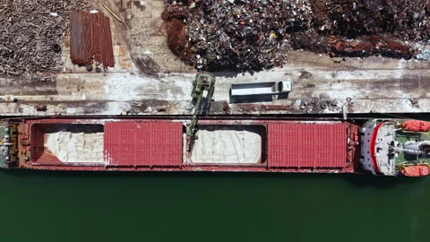 Cargo ship at port unloading materials while dock workers manage equipment in a Stock Footage 337914517