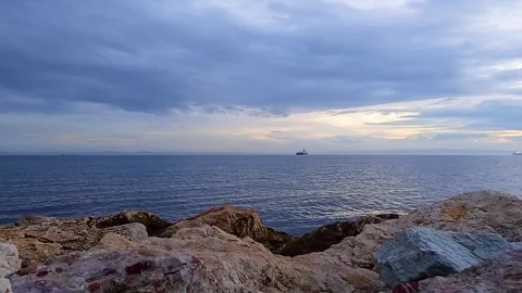 Cargo Ship Sailing on Calm Sea Under Dramatic Cloudy Sky with Rocky Coastline Video stock 333415378