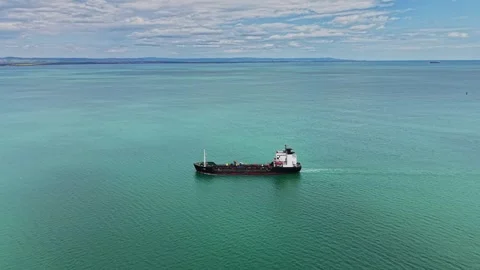 Cargo ship sails across calm sea near coastline in sunny weather 库存影片 338327912