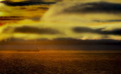Cargo ship sails across the ocean under dramatic, fiery sunset clouds 스톡 사진