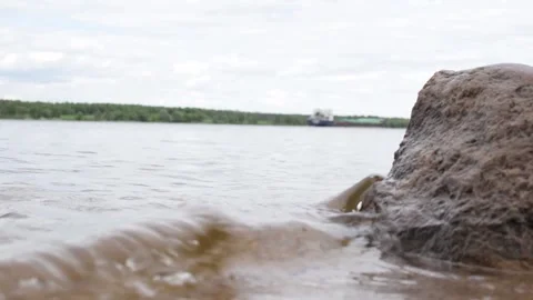 A cargo ship sails along the river in the distance, waves and sandy shore Stock Footage 198688848