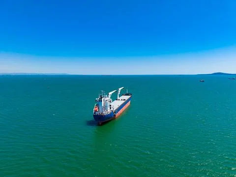 Cargo ship sails in clear blue water under bright sky near coastline with d.. Fotos Stock
