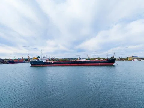 Cargo ship sails through harbor on a cloudy day with cranes in the backgrou.. Stock Photos