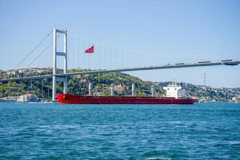 A cargo ship sails under a bridge in Istanbul on a summer and sunny day. Stock Photos
