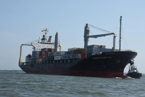 Cargo ship with shipping containers escorted by a tug boat Stock Photos