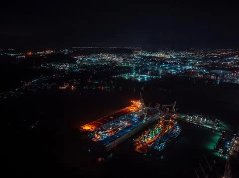 Cargo Ship Undergoing Maintenance In Illuminated Industrial Dry Dock At Nig.. 库存照片