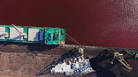 Cargo ship unloading materials at a dock on a river with dark water during 스톡 동영상 341703262