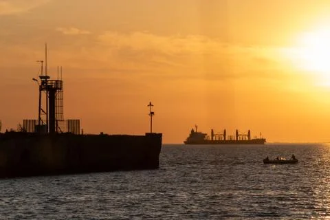 Cargo ship vs small boat with people at sunset Stock-Fotos