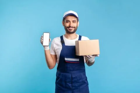 Cargo tracking mobile app. Courier man in uniform holding cardboard box and c Fotos Stock