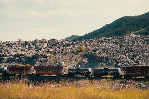 Cargo train passes through a rocky landscape with a mountain backdrop. Stock Photos