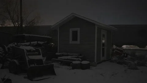 Cargo train speeding behind small building and tractor covered in snow Stock Footage 225418053
