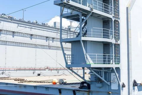 A cargo vessel is moored at the port with loading equipment visible. Workers  Stock Photos
