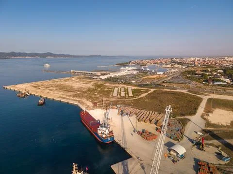 Cargo vessel rests at working harbor quay beside orderly timber stacks. Por.. 스톡 사진