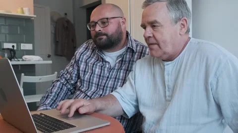 Caring adult son teaching elderly father how to use laptop, showing how to Stock Footage 282988125