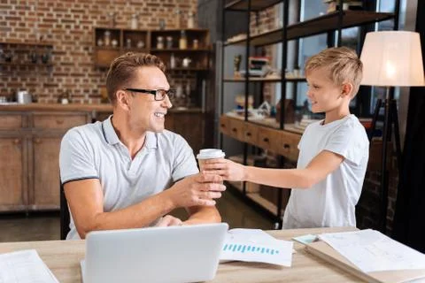 Caring boy giving his working father a cup of coffee Stock Photos
