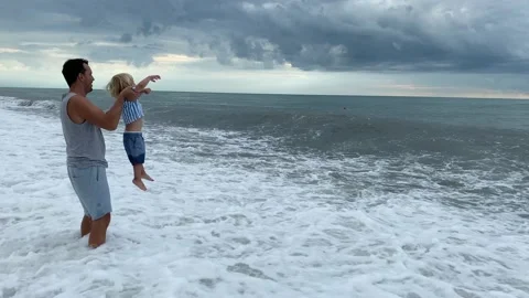 Caring father and son playing with sea waves father lifts son when wave is Video stock 229960988