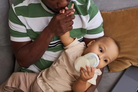 Caring father kissing tiny hand of baby son and giving him formula in bottle Stock Photos