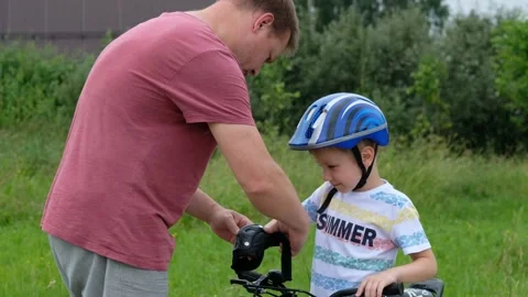 Caring father is putting elbow pad on his little son's head then teaching happy Stock Footage 134464004