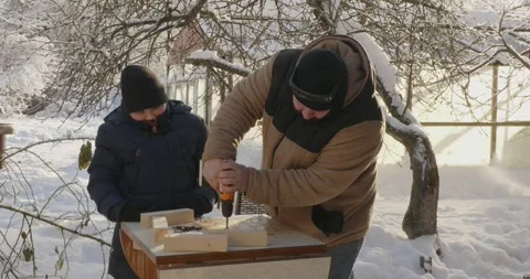 A caring father teaches his son how to build a wooden bird feeder in his snowy Video stock 332738059