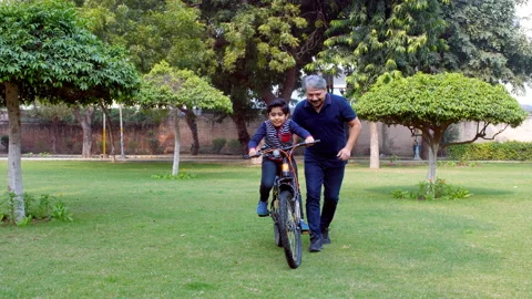 A caring father teaching his son to ride a bicycle in the public park - paren... Stock Footage 167822074