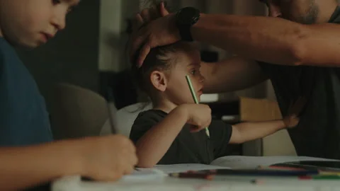 Caring father tying his daughter's hair in a ponytail while she writes in 스톡 동영상 252533677