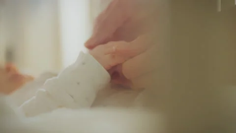 Caring hands gently hold a newborns tiny fingers in a warm nurturing environ Stock Footage 295127047
