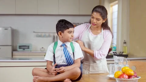 Caring Indian mother preparing kid for school by placing lunch box and water in Stock Footage 263796276
