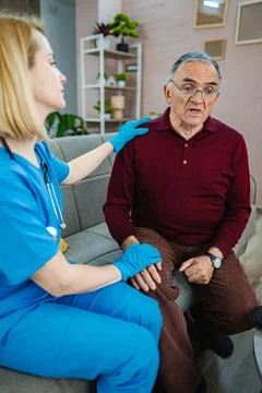 Caring interaction between nurse and elderly man at home Stock Photos