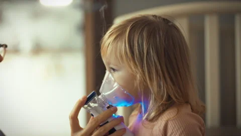 Caring mom administers medication treatment to her child using a nebulizer d Stock Footage 331303223