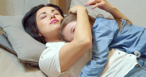 Caring mother hugging and caressing her little daughter lying on the sofa Stock Footage 131823619