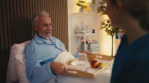 Caring nurse bringing breakfast to bed-bound aged patient of a retirement home Stock Footage 279177424