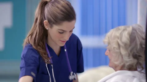 Caring nurse chats with an elderly female patient on a hospital ward. Stock Footage