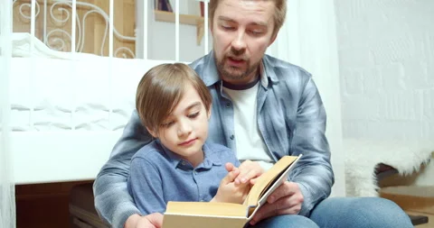 Caring parent dad is reading interesting book to his little son at home. Stock Footage 131682175