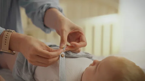 Caring parent gently dressing a baby in a cozy nursery during morning routin Stock Footage 291434170