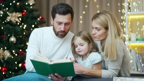 Caring parents are reading a book to their little daughter in a cozy house on Stock Footage 219902936