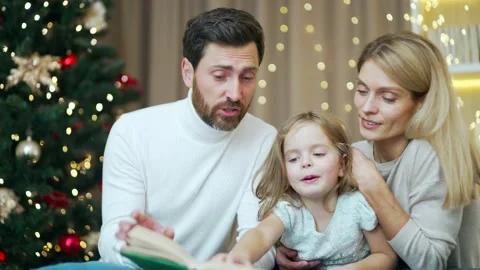 Caring parents are reading a book to their little daughter in a cozy house  Stock Footage 219913893