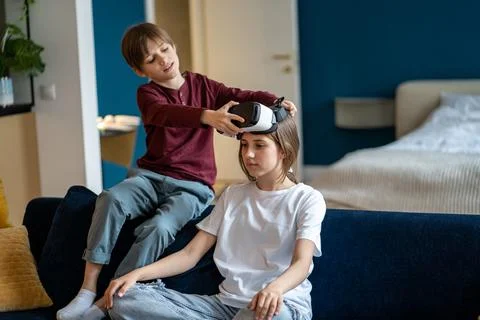 Caring small brother help curious teenage girl put on virtual reality glasses Stock Photos