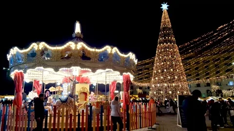 Carousel spins beside a light-covered Christmas tree at a bustling night market Video stock 332269739