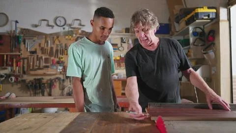 Carpenter and apprentice working at workshop, teacher orienting young man w.. Stock Photos