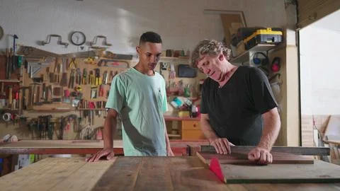 Carpenter and apprentice working at workshop, teacher orienting young man w.. Stock Photos