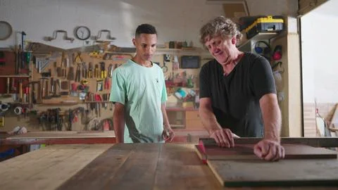 Carpenter and apprentice working at workshop, teacher orienting young man w.. Stock Photos