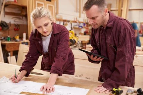 Carpenter With Apprentice Looking At Plans In Workshop Stock Photos