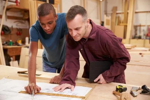 Carpenter With Apprentice Looking At Plans In Workshop Stock Photos